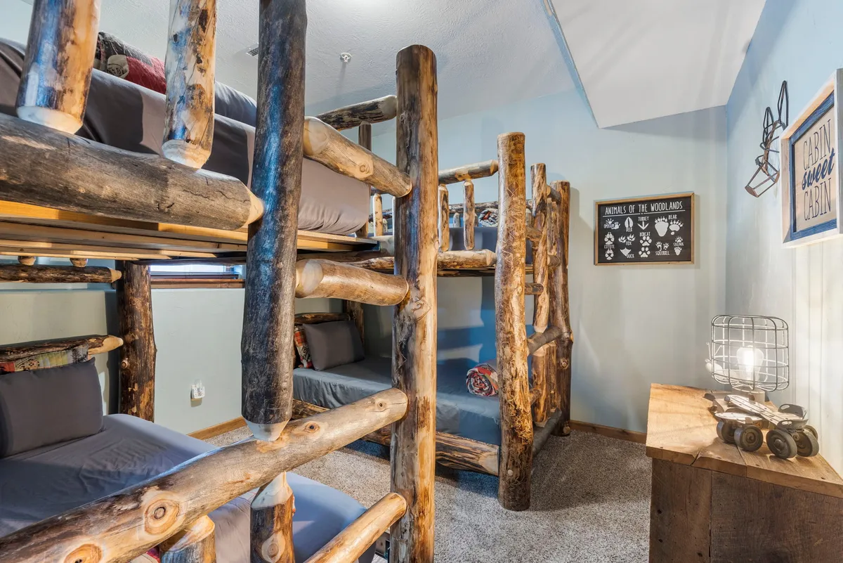 A playful bunk room featuring log-frame bunk beds, whimsical wall art, and a wooden nightstand with a lamp. The space is designed to evoke fun and togetherness, ideal for children or groups of friends having a sleepover adventure.