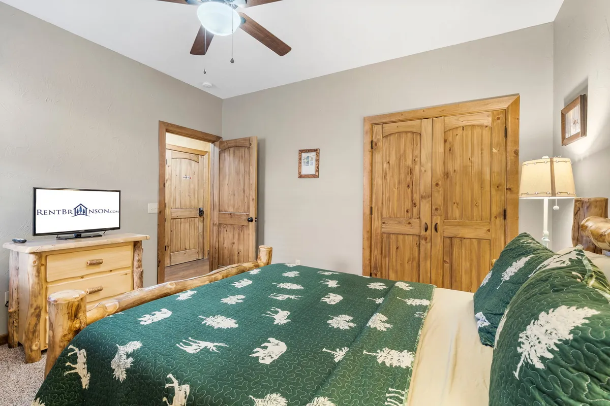 A cozy queen bedroom with a patterned blanket on the bed, sturdy wooden furniture, and a television for entertainment. The setting is warm and inviting, ideal for winding down with a movie or enjoying morning coffee in bed.