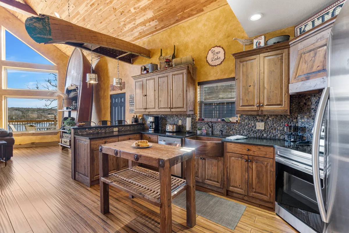 A bright, airy kitchen with rustic cabinetry and a central island, complemented by large windows overlooking the lake. A wooden canoe hangs playfully from the ceiling, hinting at lakeside adventures and family fun.