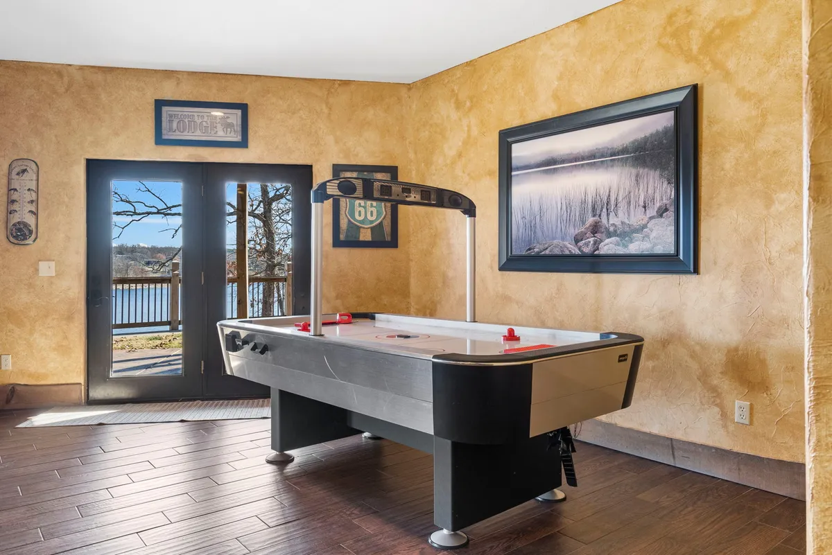 A fun, relaxed room with a large air hockey table at center, set in front of expansive windows overlooking scenic views. The space is designed for socializing and energetic play, inviting groups to gather for friendly competition with nature as the backdrop.