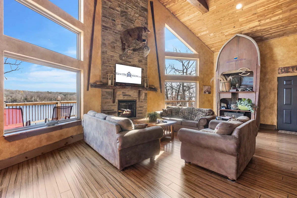 A spacious, inviting interior with a stone fireplace, large windows looking out to nature, and comfortable seating. The room feels cozy and offers plenty of space for both people and pets to relax indoors, enhancing the feeling of a home-away-from-home for all family members.